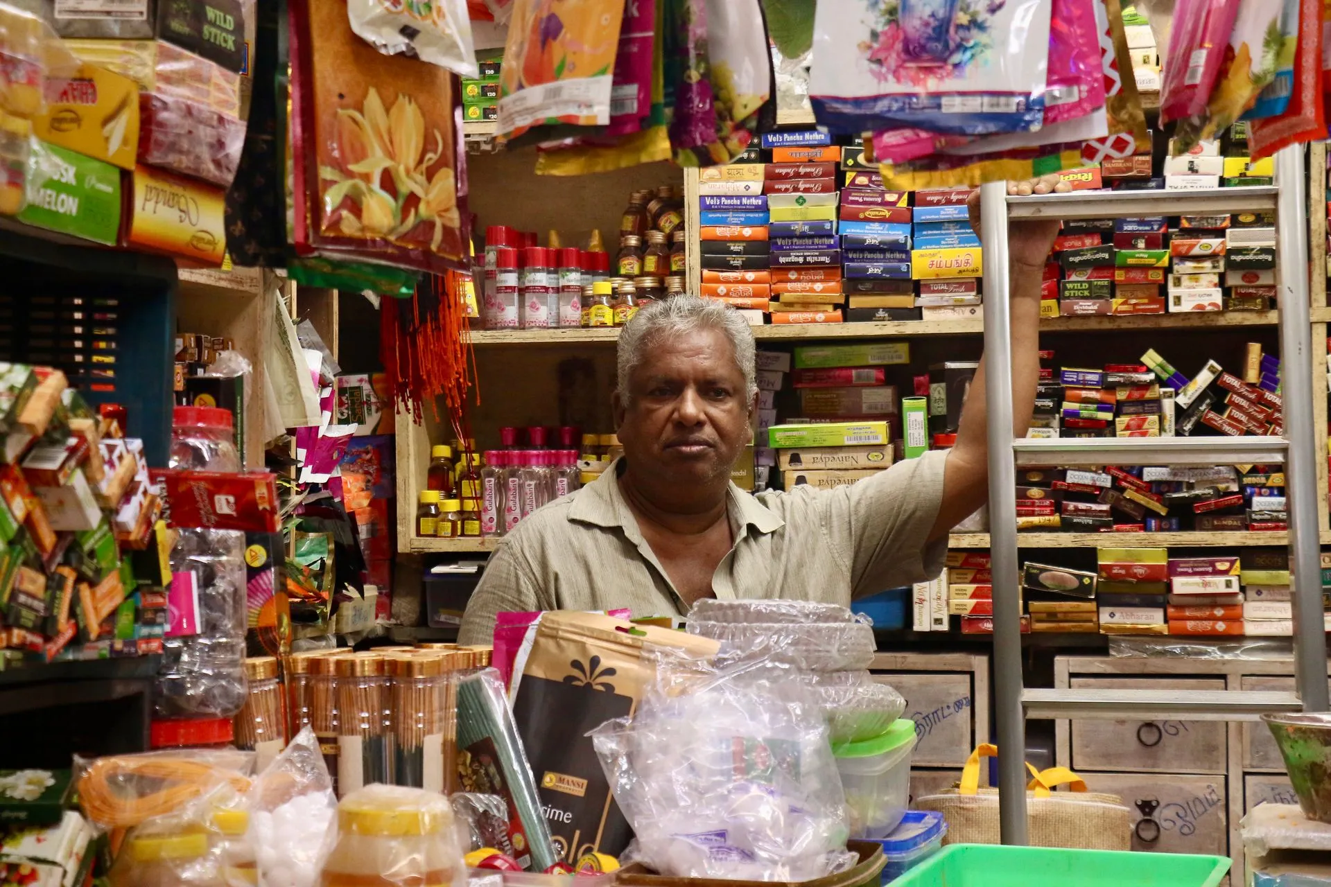 Indian shopkeeper standing at the counter of a well-stocked neighbourhood store