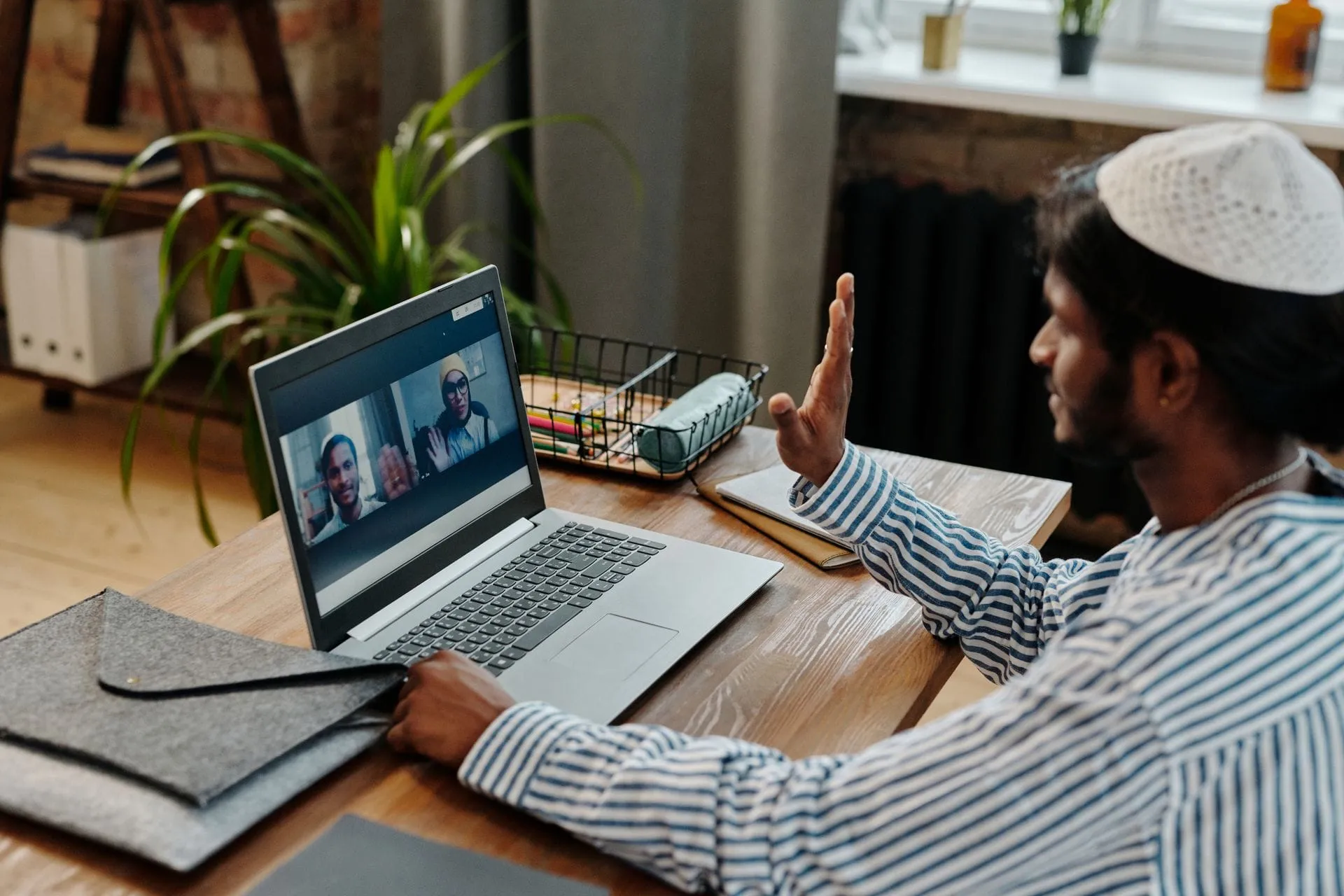 Indian man waving to colleagues on a video call from his laptop